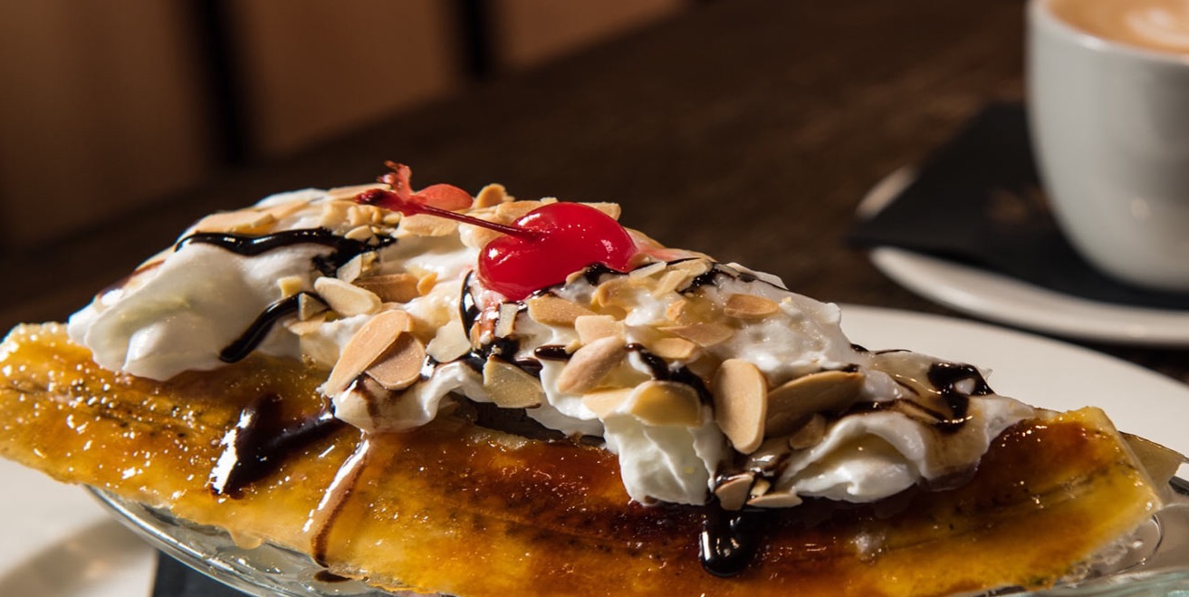a banana topped with whipped cream, chocolate and a cherry and nuts