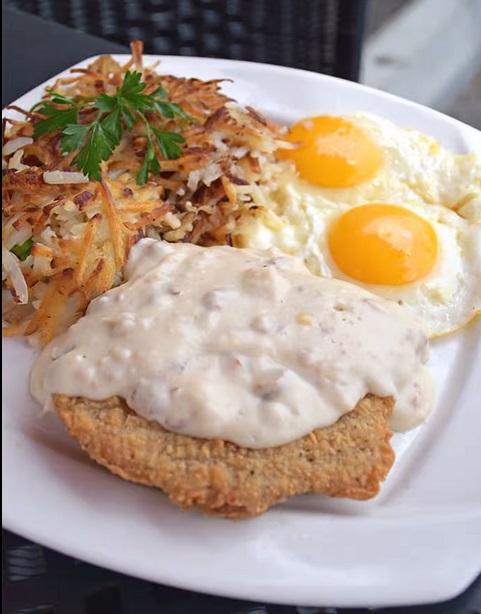 chicken fried steak topped with gravy, two eggs to the side and hash browns with green garnish on top